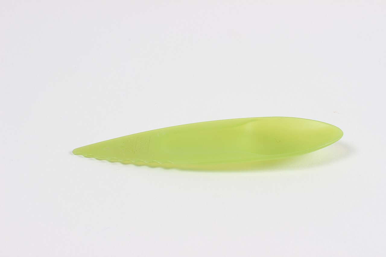 Kiwifruit spoon-knife; green plastic; elongated oval with spoon indentation at end and serrations on one side of handle; engraved logo.